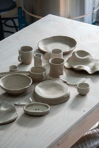 Raw stoneware tableware set of wheel-thrown cups, plates and bowls on a wooden table.